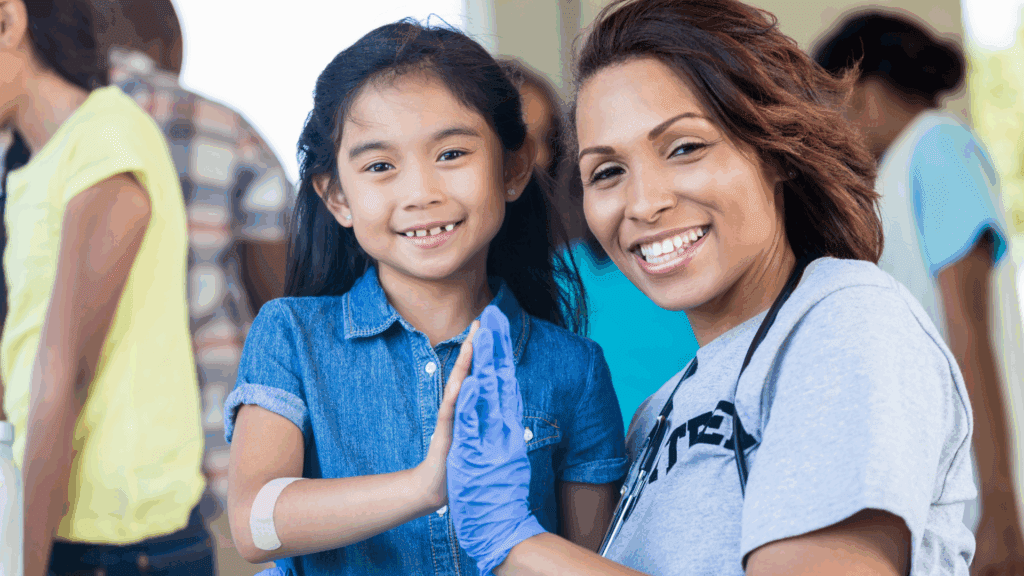 Volunteer high-fives a smiling child at a community event, blue glove and bandage visible—mentor moment.