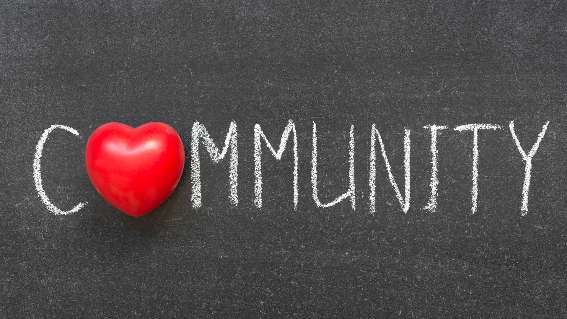 The word Community in white chalk with a red heart, highlighting local support and belonging.