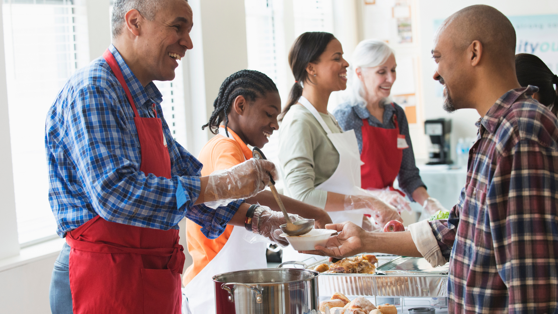 Smiling volunteers of different ages serving soup at a community meal, showing hands‑on service and care.
