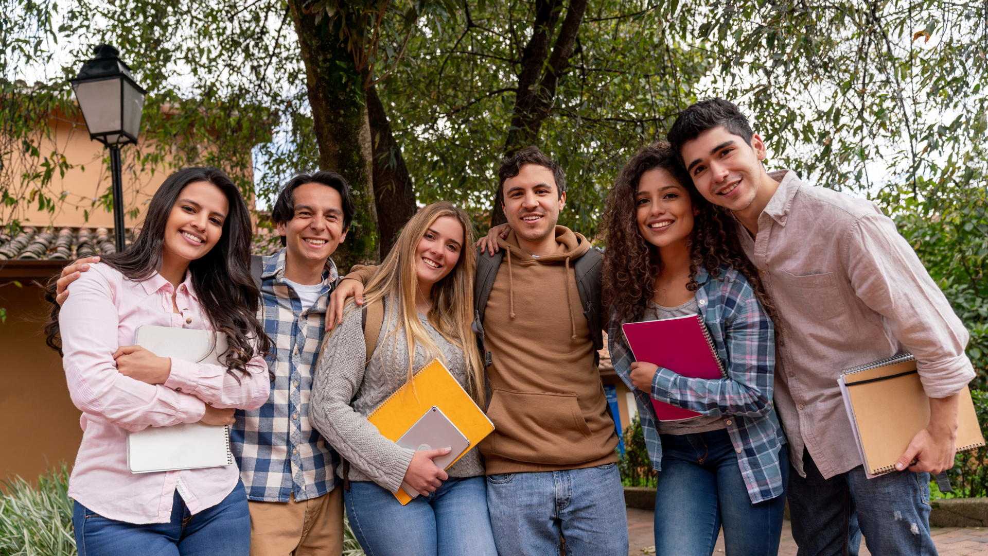 Diverse teens standing arm in arm outdoors with notebooks, representing youth leadership and mentoring.