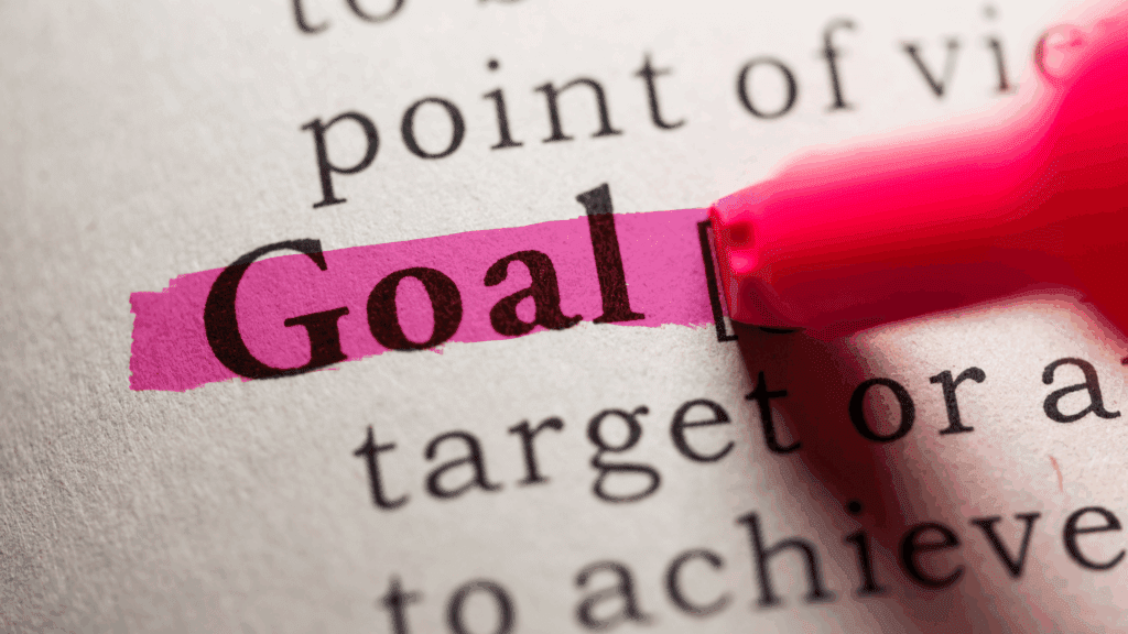 Close-up of a dictionary page with the word “Goal” highlighted in pink by a marker.