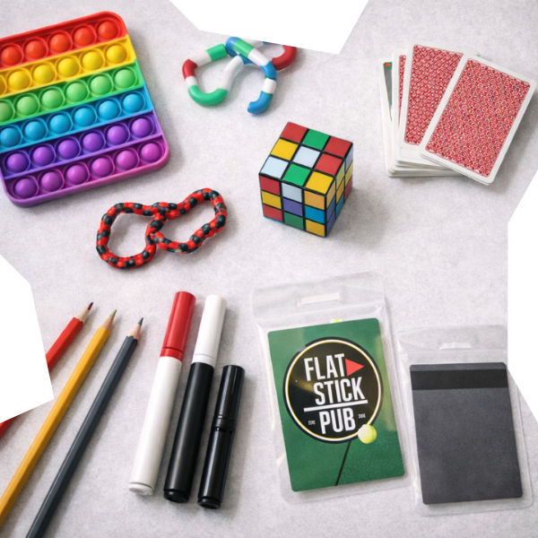 Flat-lay of enrichment items for teens including fidget toys, a puzzle cube, playing cards, art supplies, and a Flat Stick Pub gift card, arranged on a light background to suggest play, connection, and stress relief.